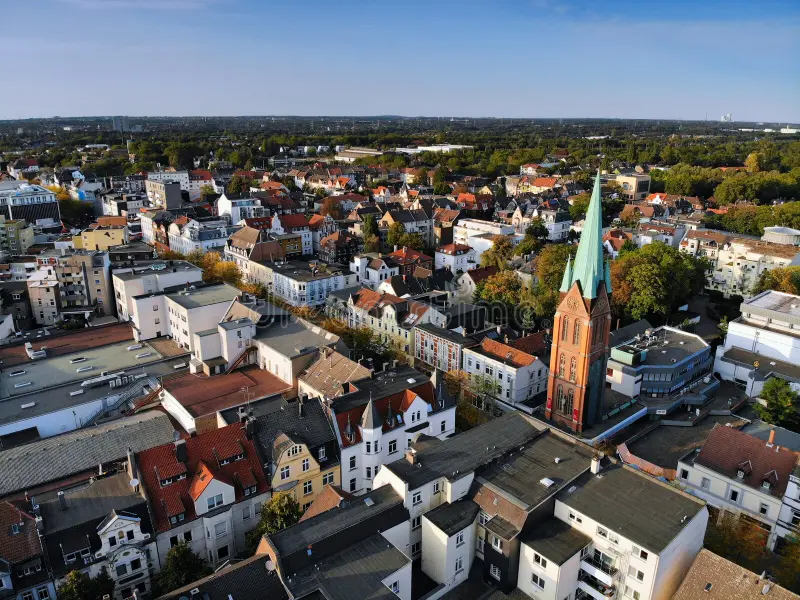 Luftaufnahme einer Stadt mit vielen Häusern und einem markanten Kirchturm in der Mitte.
